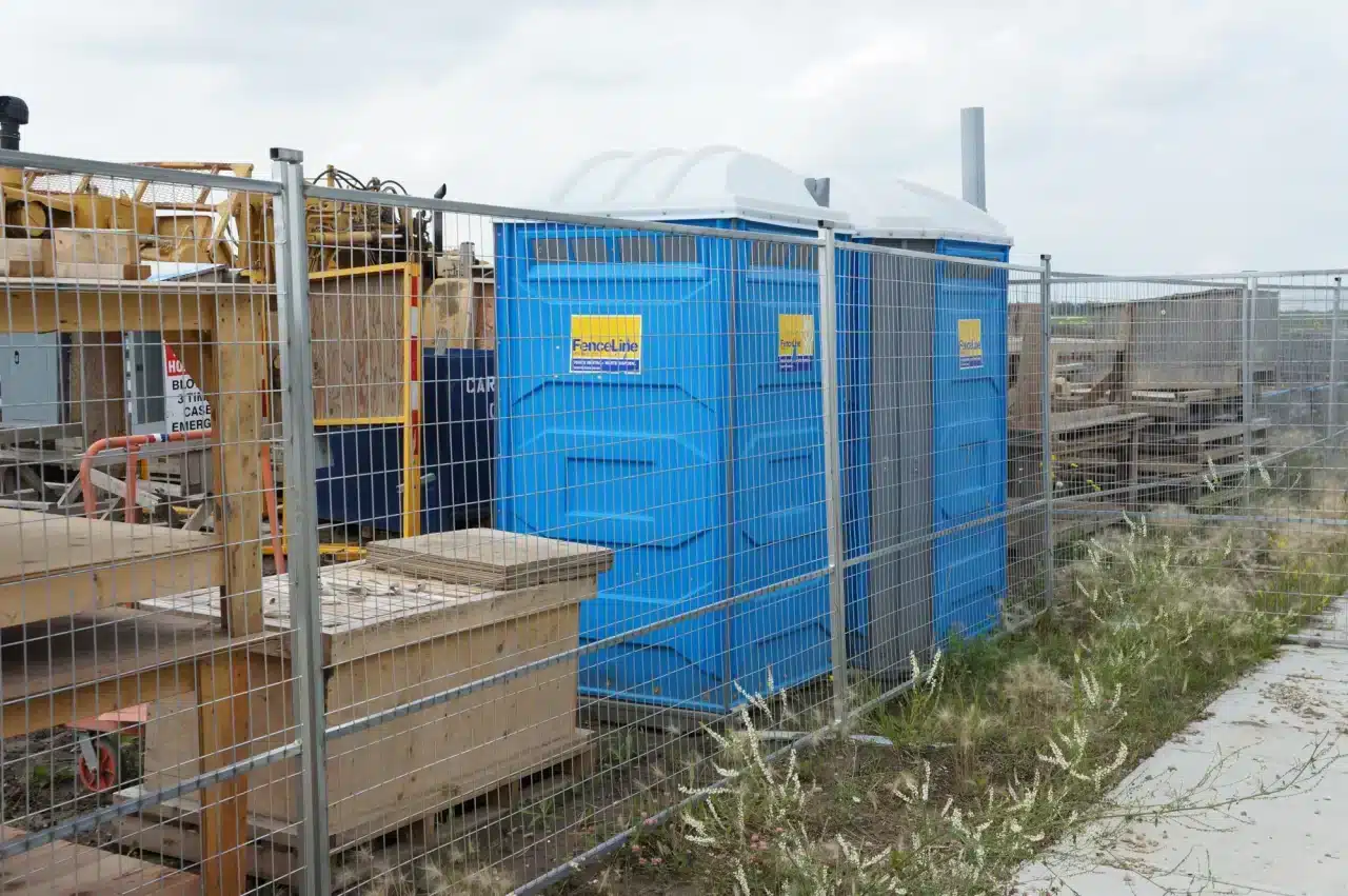 A construction fence surrounding a site in Alberta, securing equipment and porta potties.