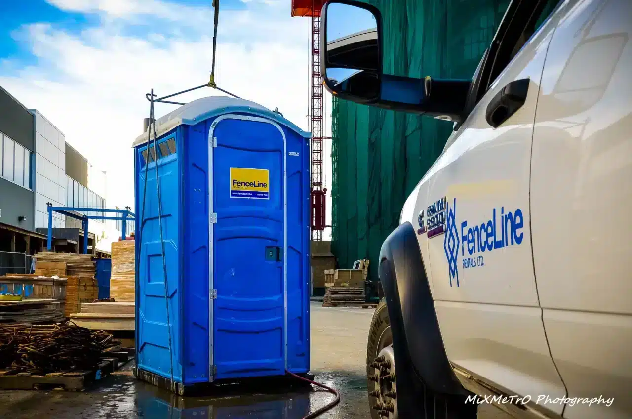 A portable toilet is lowered onto a construction site in Alberta by a crane.