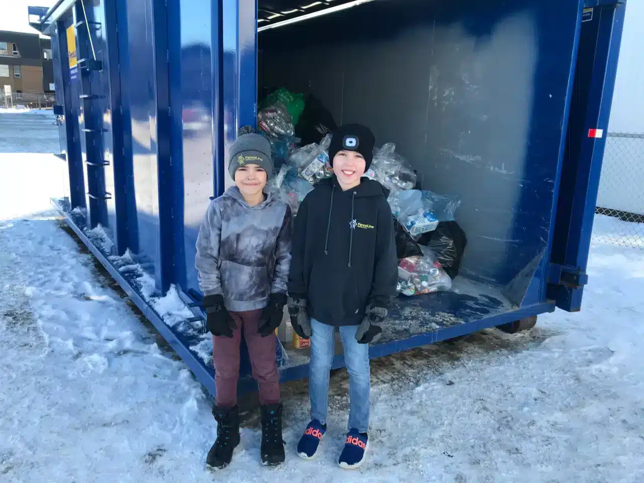 Two kids help fill up a large waste bin with bottles for a bottle drive.