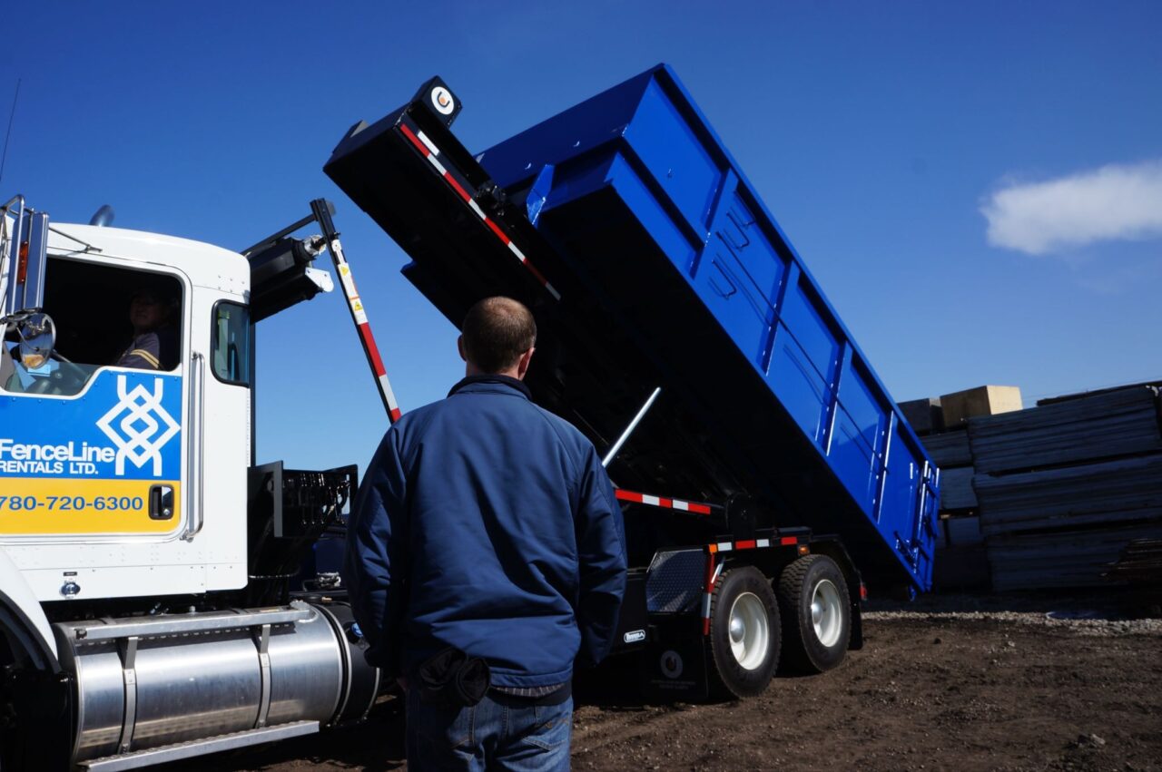 A truck backs up to empty a large waste bin at a construction site.