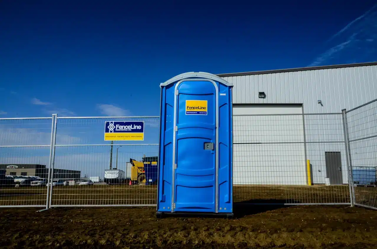 a portable toilet and a temporary fence from FenceLine ready to be rented for an outdoor event in Edmonton.