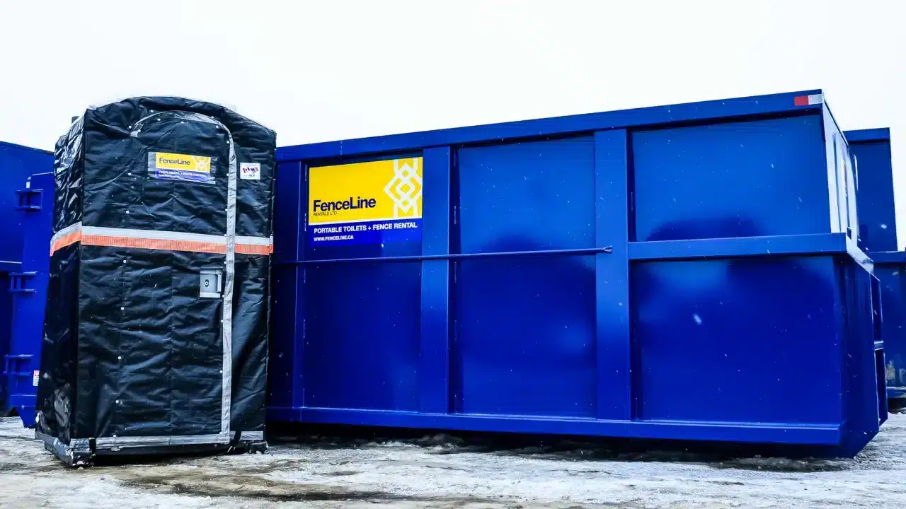 A jacketed porta potty next to a large waste bin on a remote construction site in Alberta.