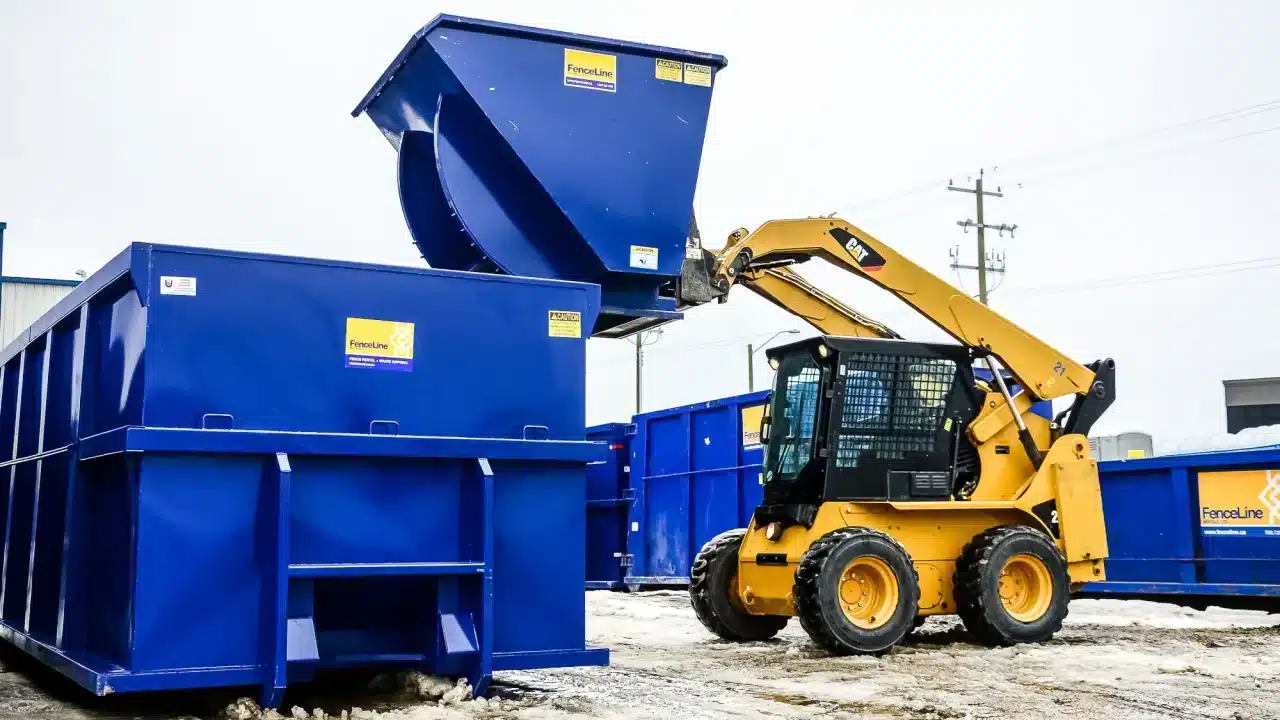 A forklift dumps a smaller waste bin into a larger one on a remote construction site in Alberta.