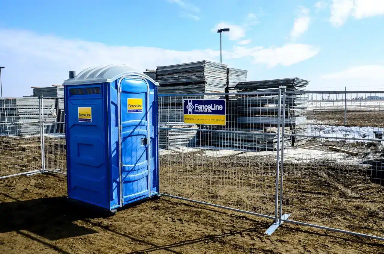 A portable toilet in front of a stack of temporary fencing in Edmonton