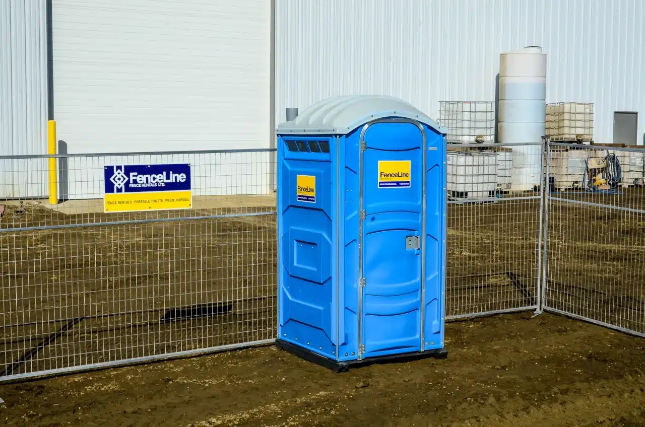 A portable toilet stands in front of a temporary fence setup in Edmonton