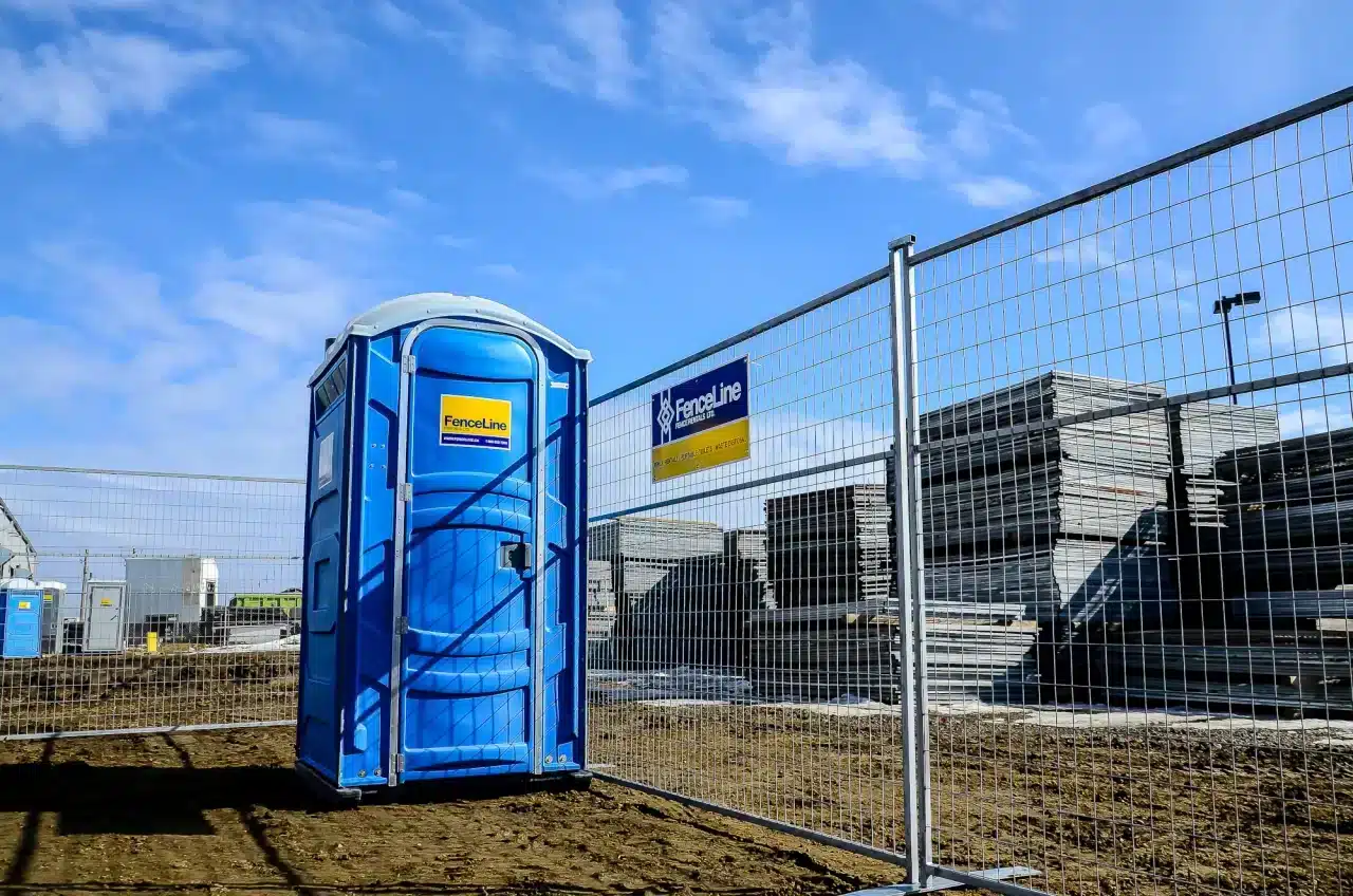 A portable toilet stands next to a construction fence on a site in Edmonton.