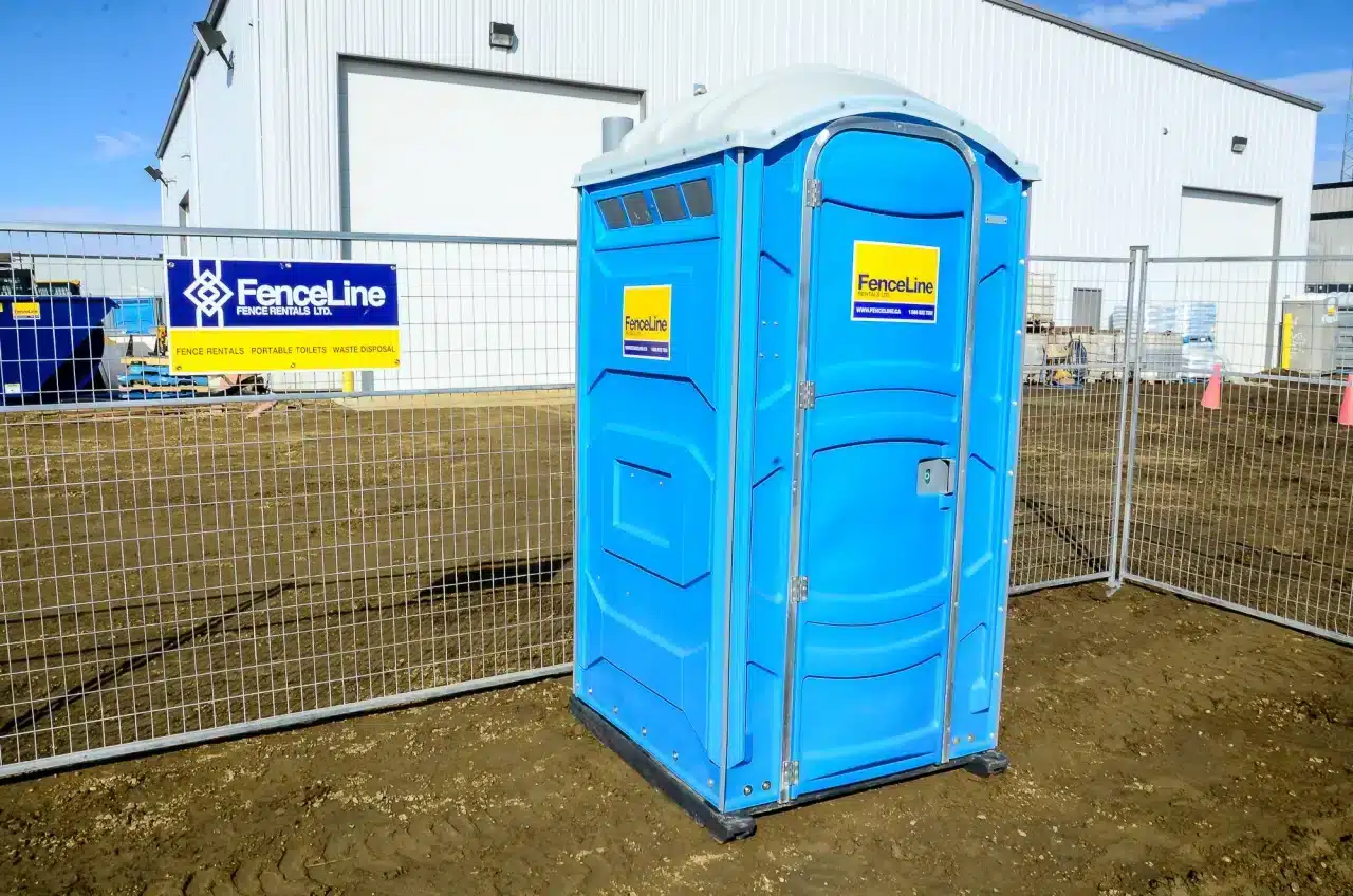 A temporary fence and portable toilet stand in an industrial site in Edmonton.