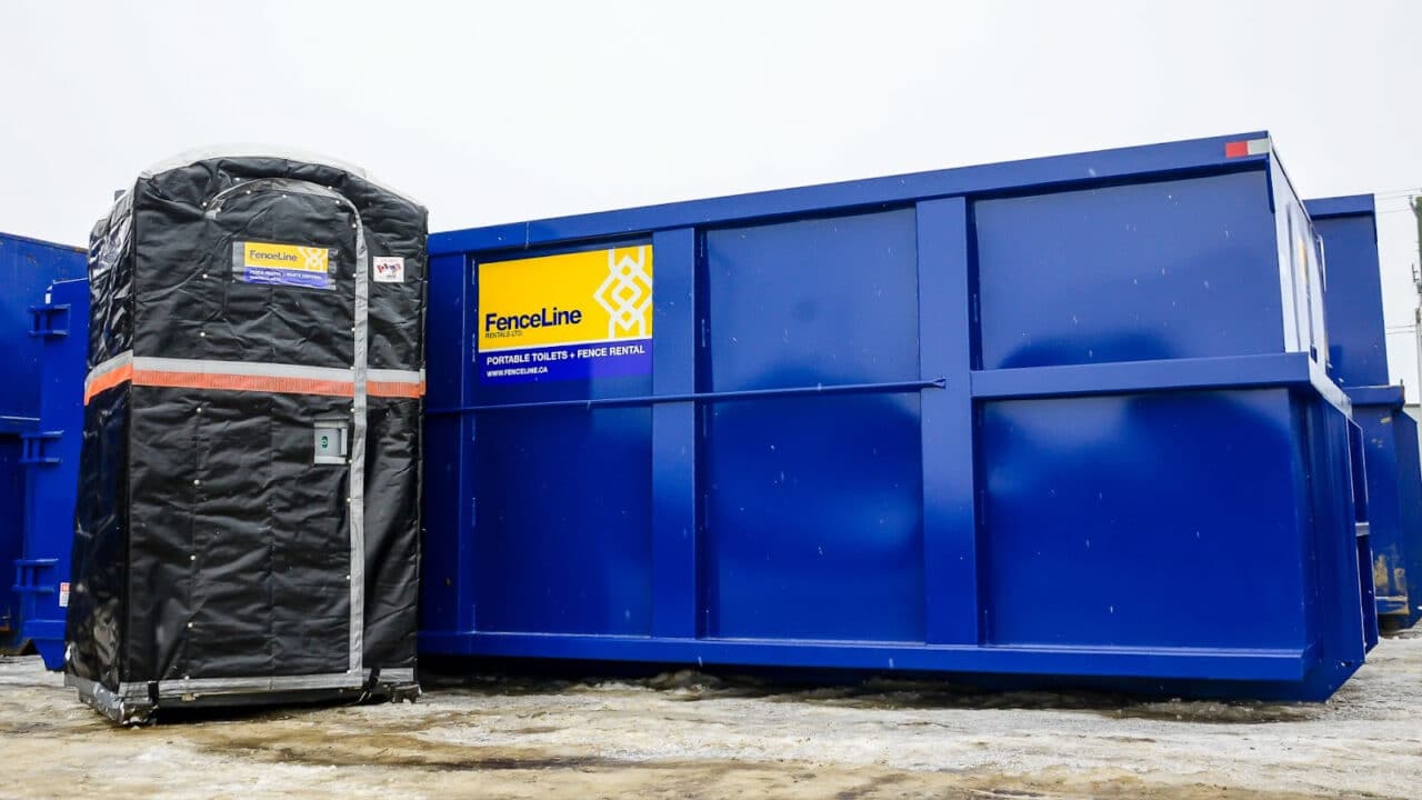 A winterized portable toilet with a sleeve stands next to a waste bin on an industrial site in Edmonton.