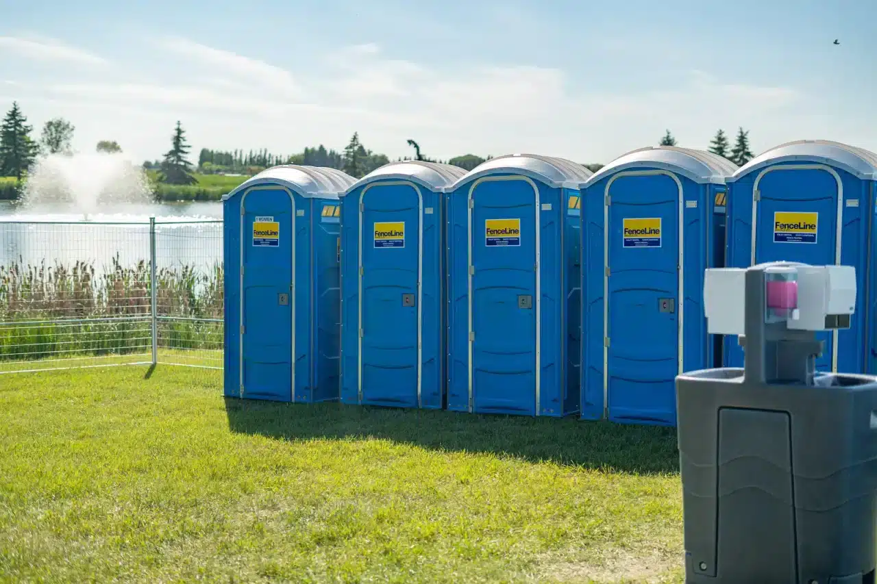 A row of portable toilets at an outdoor event in Alberta with a handwashing station nearby.