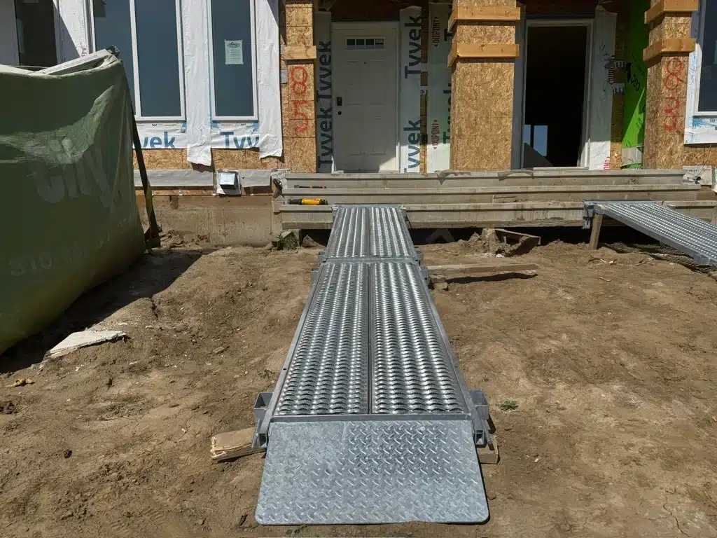 A walkway plank leads over the ground in front of a home construction site in Alberta.