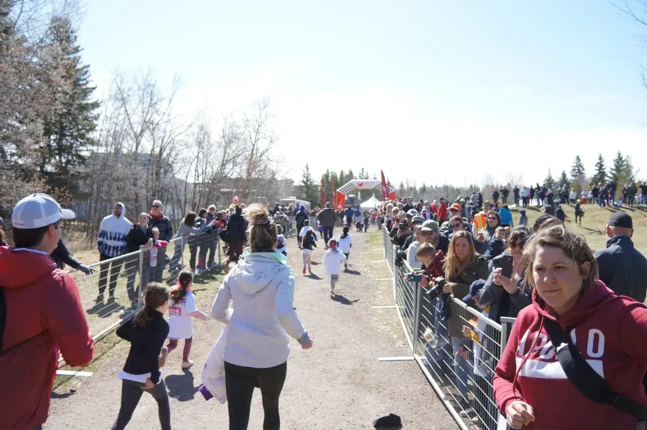 People stand oudtside crown control barriers while kids and parents participate in a fun run.