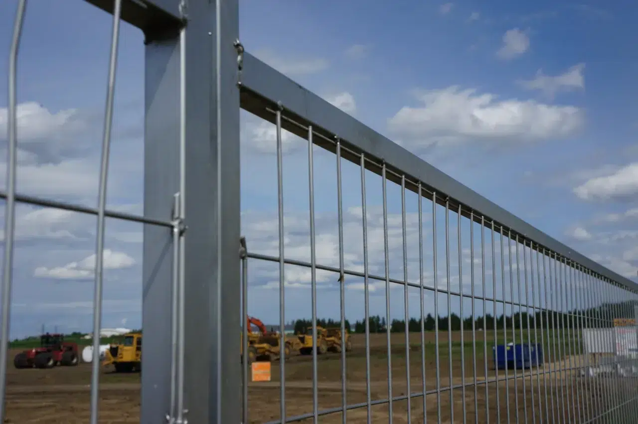 A heavy-duty fence surrounds a large field with heavy machinery in Alberta.