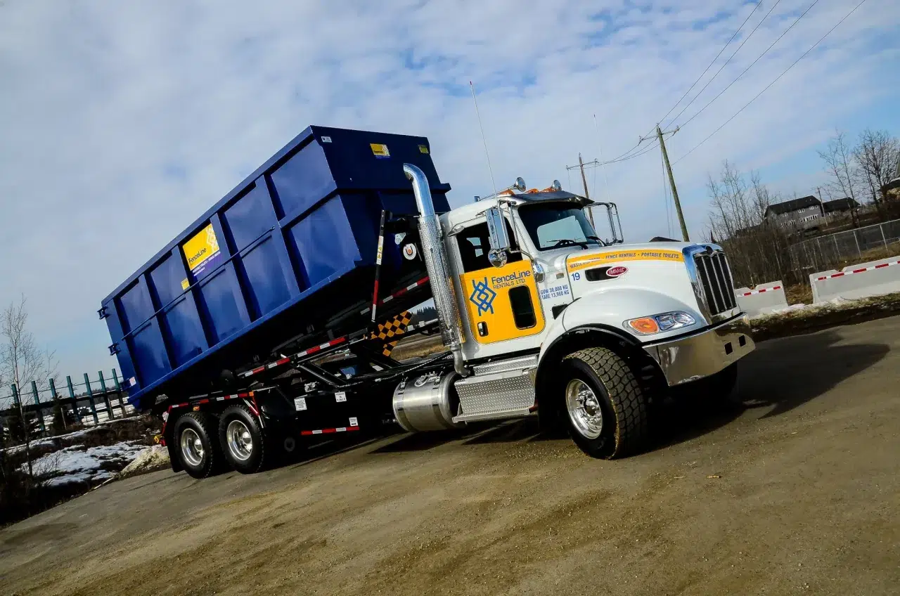 A fenceline truck delivers a blue waste bin that was rented for a demolition project in Alberta.