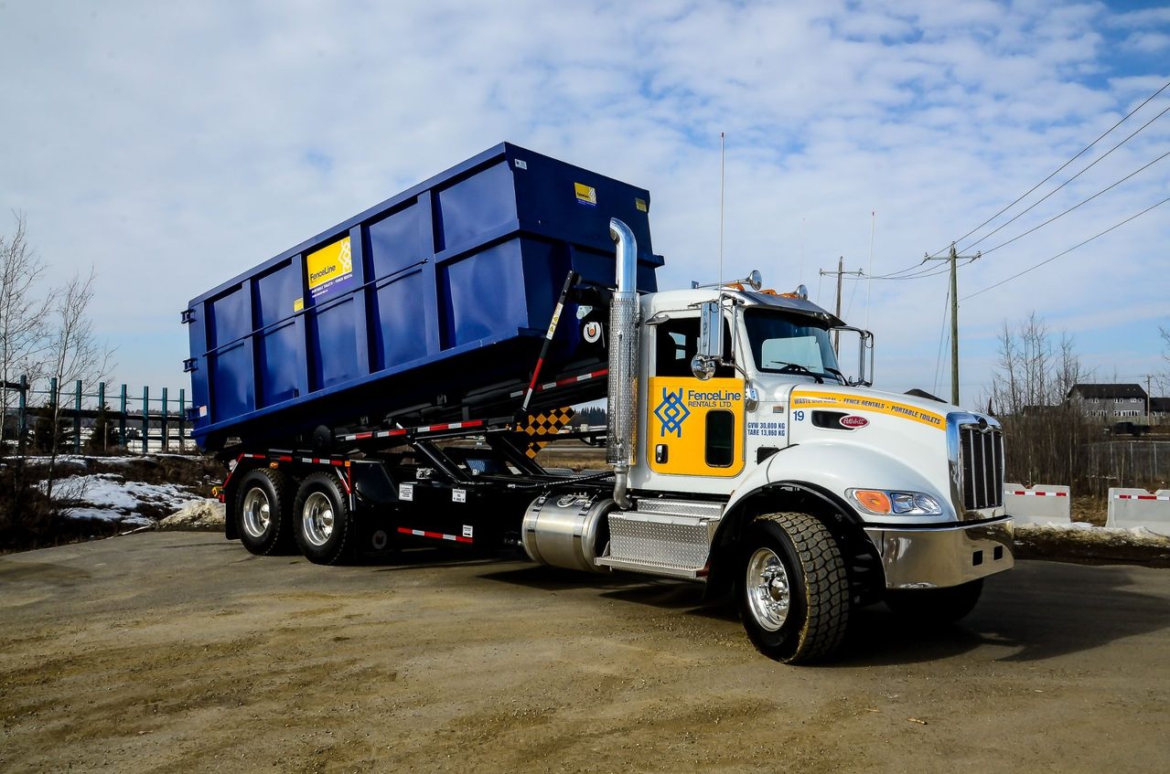 A fenceline truck arrives on a construction site in Calgary to deliver a large waste bin.