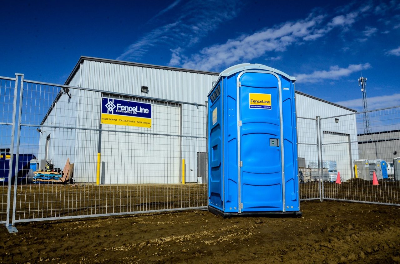 A fenceline porto potty against a fence on a work stie in Calgary.